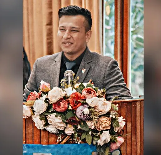 Ankush Kurkalang speaking at a flower-decorated podium at a Rotary Club event